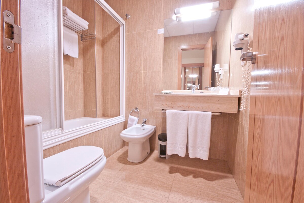 A modern bathroom with a toilet, bidet, sink, and mirror.