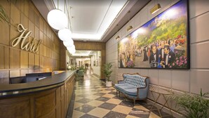 Vestíbulo de hotel con recepción, mostrador de entrada, zona de registro, área de descanso y un cuadro grande en la pared.