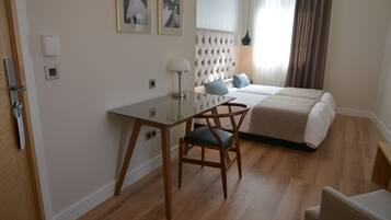 Een hotelkamer met een bed, een bureau en een stoel. Twee ingelijste foto’s hangen aan de muur, evenals een lamp en een raam met gordijnen.