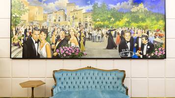 A large painting of a formal event in a square with buildings and a castle in the background, a blue sofa, and a small wooden table in the foreground.