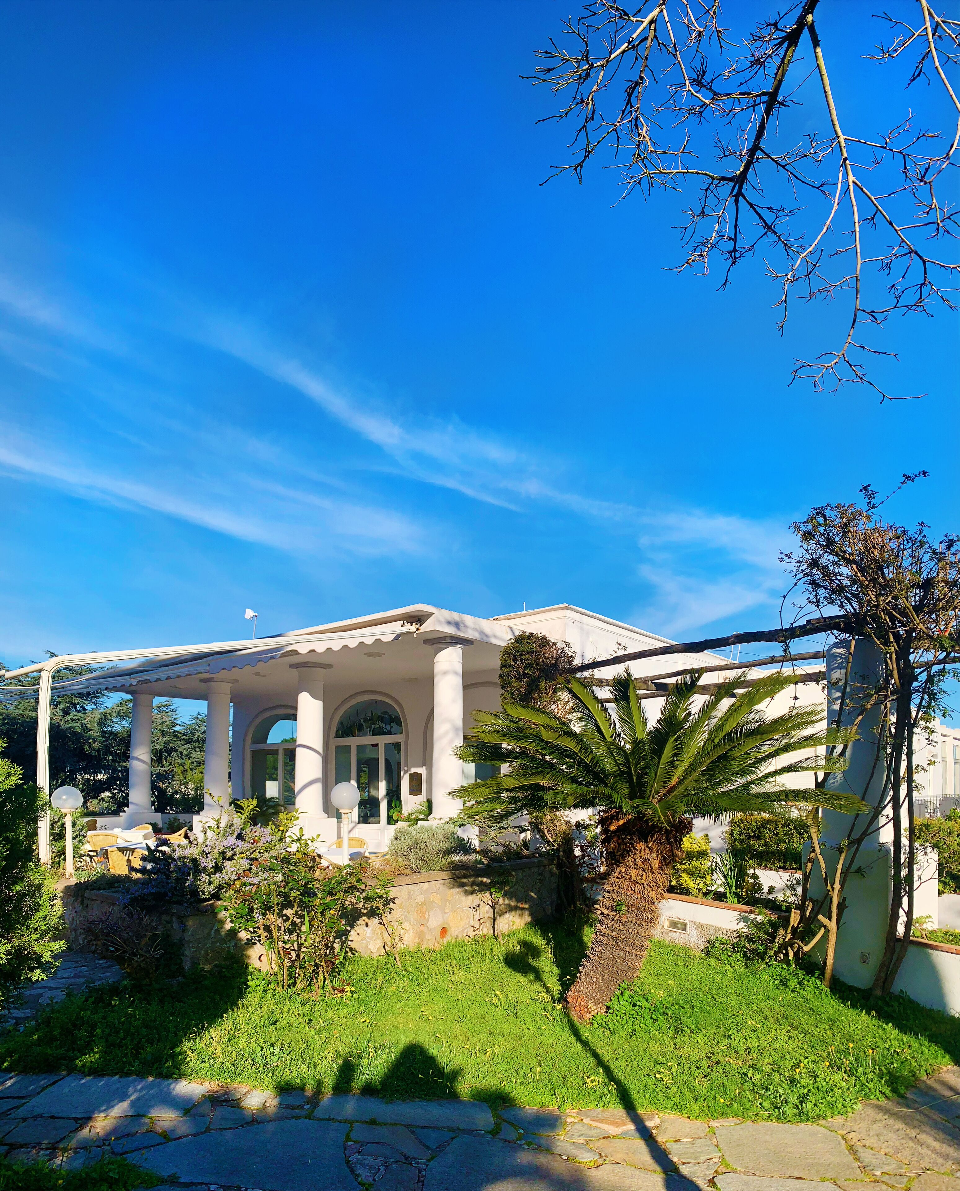 A white building with a covered patio, surrounded by greenery and a clear blue sky.