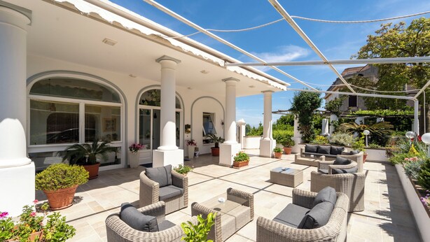 An outdoor patio with wicker furniture, potted plants, and a pergola. - Hotel Bellavista (Anacapri)