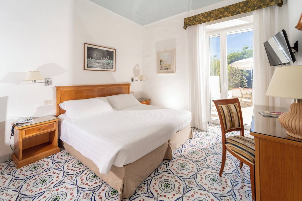 A hotel room with a bed, a chair, a desk, and a TV.