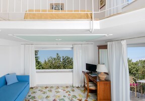 Ein Zimmer mit einem blauen Sofa, einem Schreibtisch mit Computer, einem Stuhl und einem Fenster mit Vorhängen.
