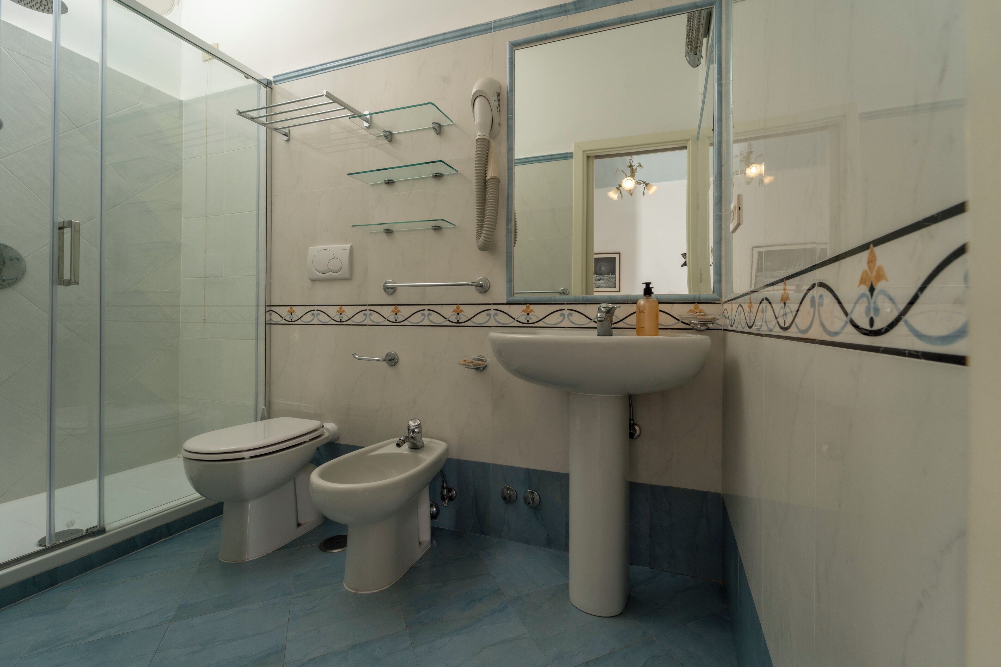 A bathroom with a glass shower enclosure, a toilet, a bidet, a sink, and a mirror.
