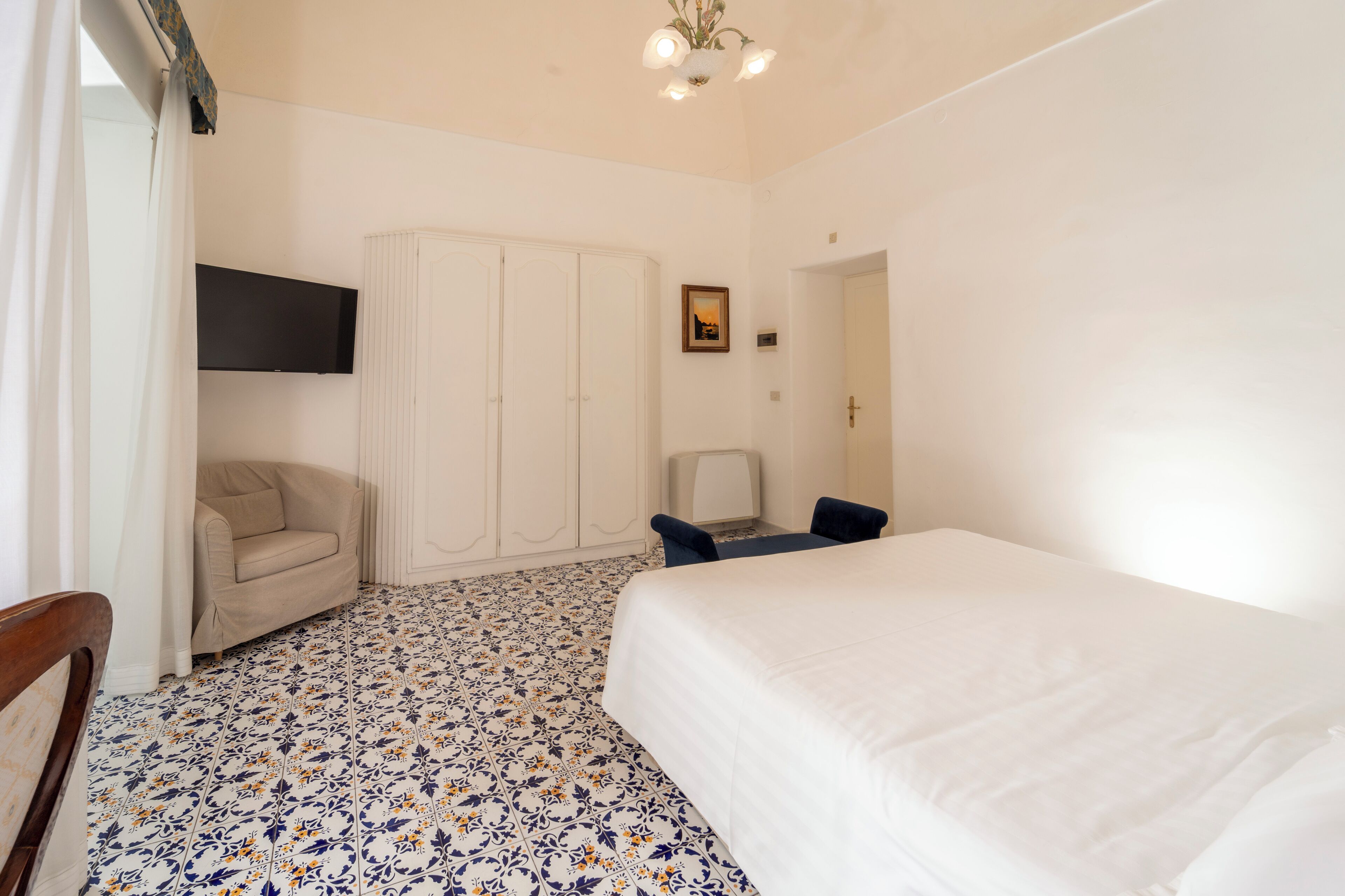 Un dormitorio con cama, una silla, un armario y un televisor montado en la pared.
