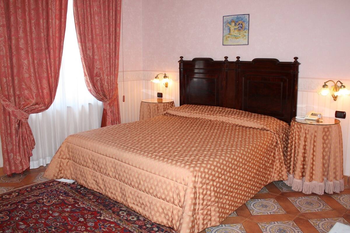 A bedroom with a large bed, two bedside tables with lamps, a patterned rug, and a painting on the wall.