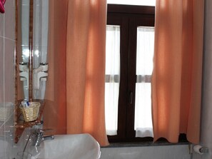 A bathroom with a bathtub, a sink, and a mirror. There is a wicker basket on the counter and a toilet paper roll visible. - Hotel Baglio Conca D'Oro (Palermo)
