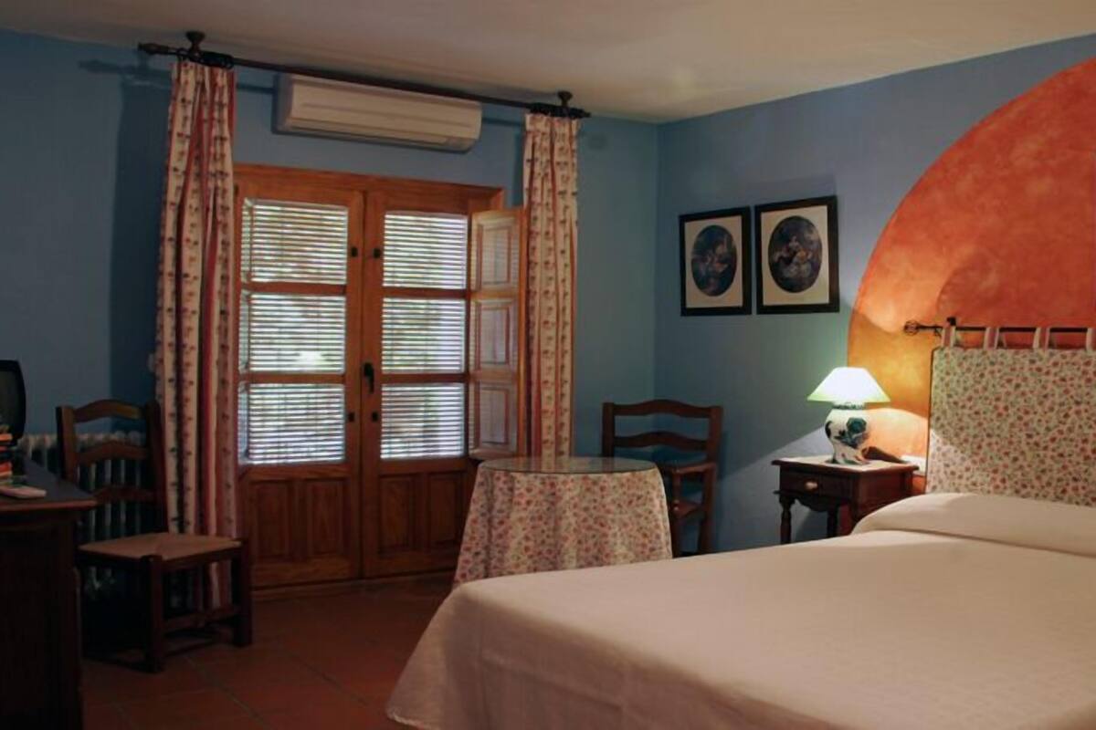 Un dormitorio con cama, escritorio, silla, mesa y ventana con cortinas.