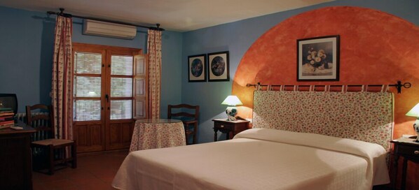 A bedroom with a bed, a desk, a chair, a table, and a window with curtains.