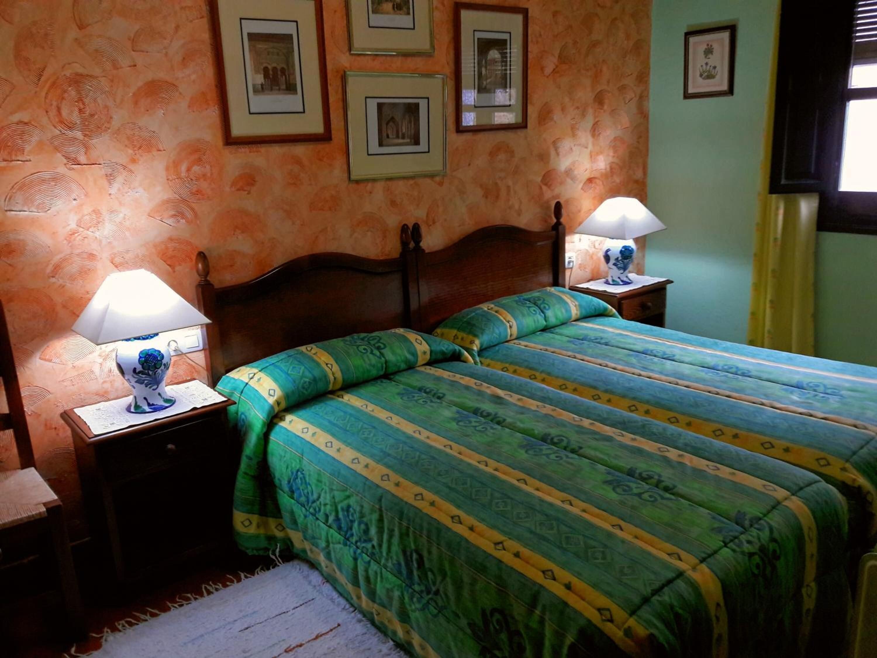 A bedroom with a wooden bed, green and blue bedding, two bedside lamps, and framed pictures on the wall.