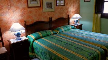 A bedroom with a wooden bed, green and blue bedding, two bedside lamps, and framed pictures on the wall.