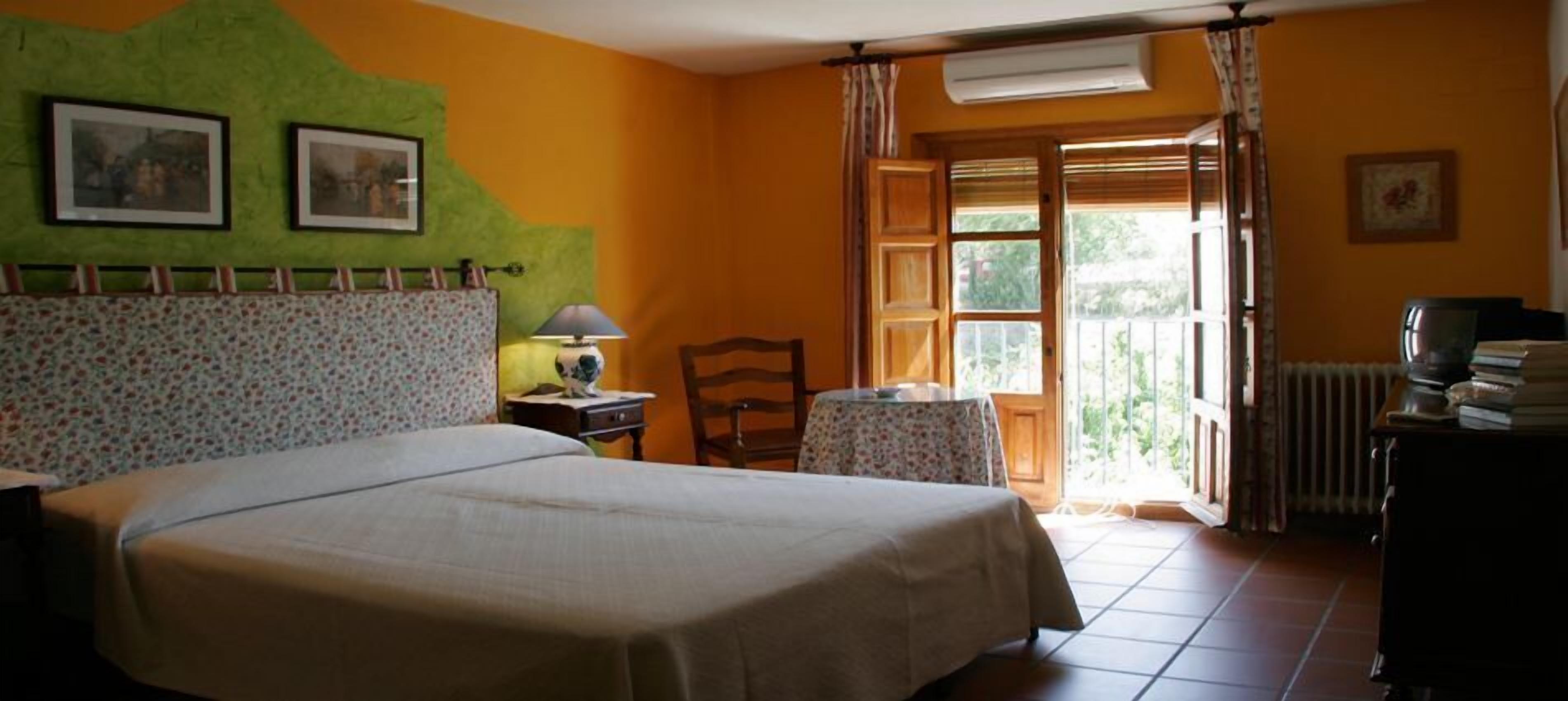 Un dormitorio con cama, una silla, una mesa y una ventana con cortinas.