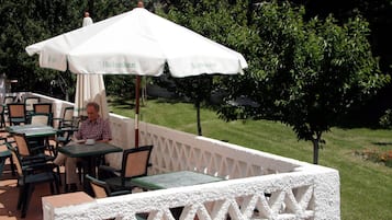 An outdoor patio with tables and chairs, a white umbrella, and a person seated at a table.