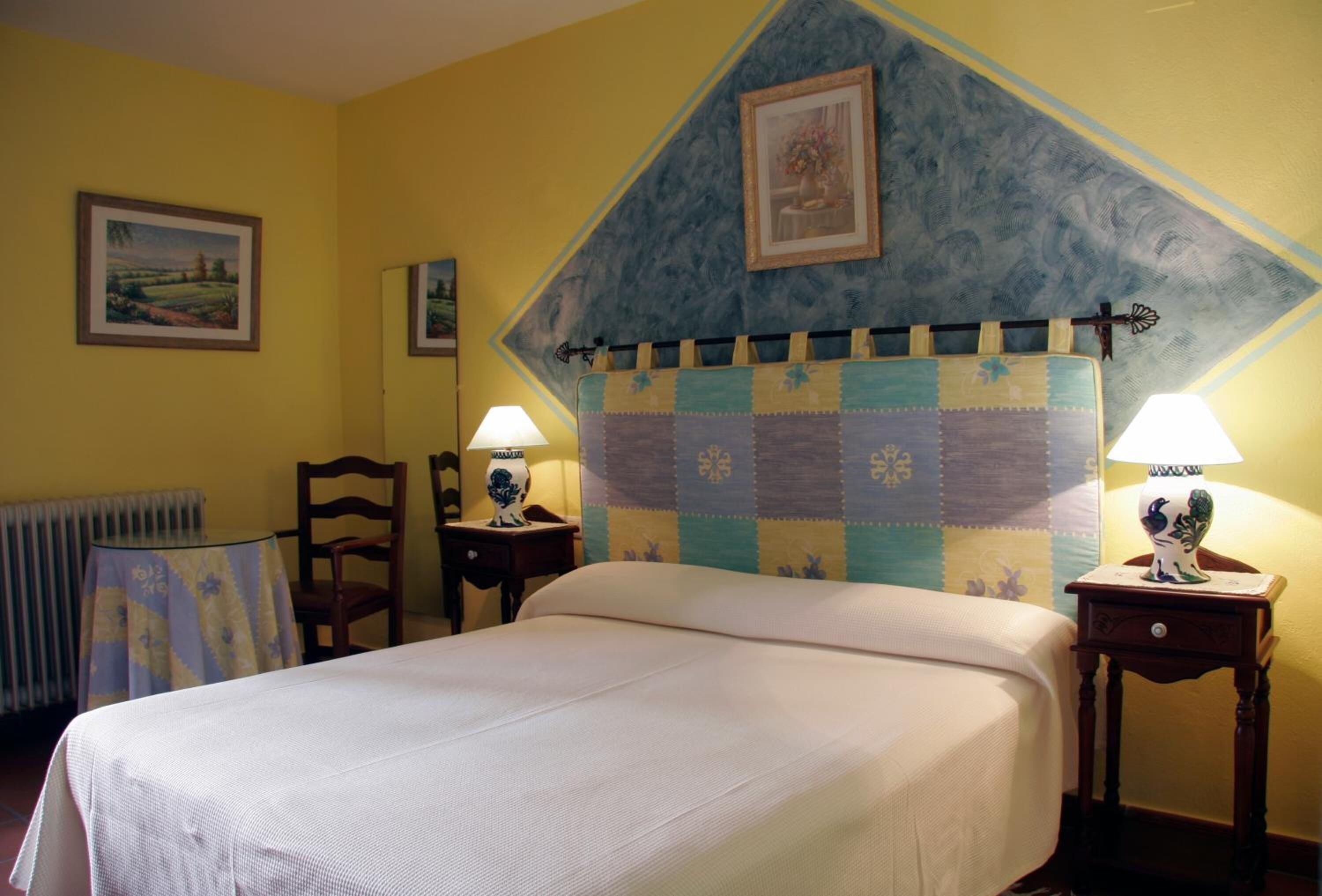 Une chambre à coucher avec un lit, deux tables de chevet avec des lampes, une chaise et un radiateur.