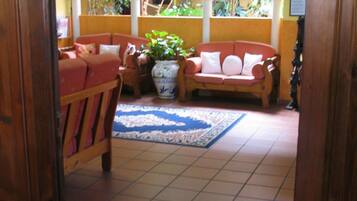 A cozy living room with a red sofa, a wooden bench, and a blue patterned rug. There is a large window with arches and a view of greenery outside.
