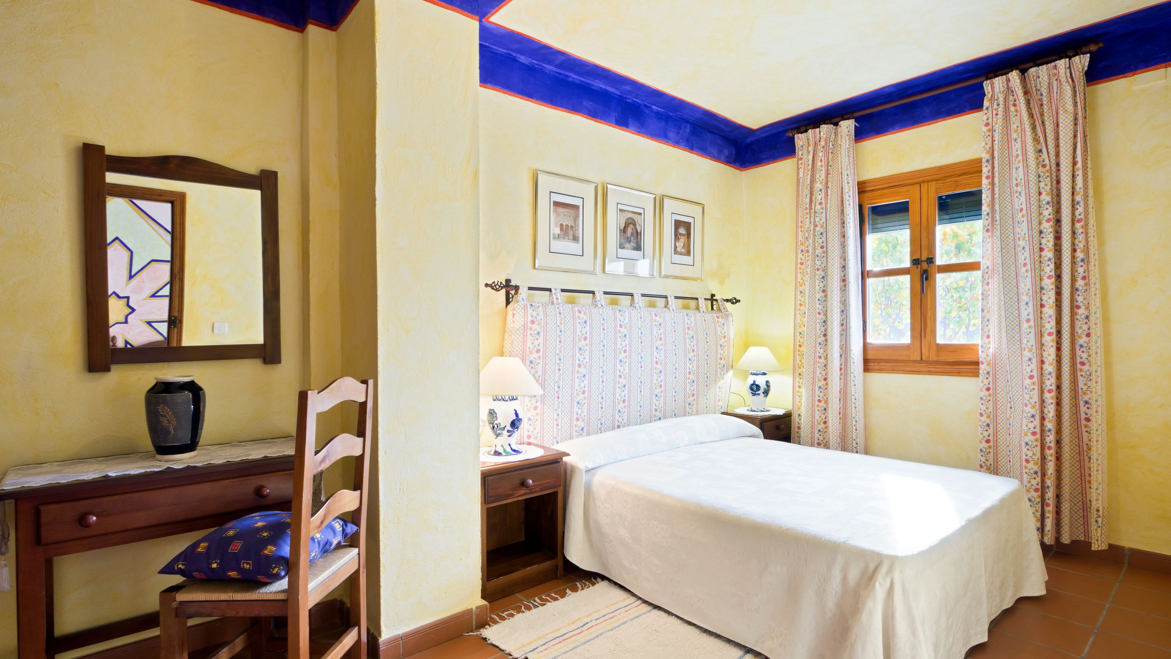 Un dormitorio con cama, escritorio, silla, lámpara y ventana con cortinas.