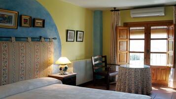 A bedroom with a bed, a nightstand with a lamp, a chair, a round table, and a window with curtains.