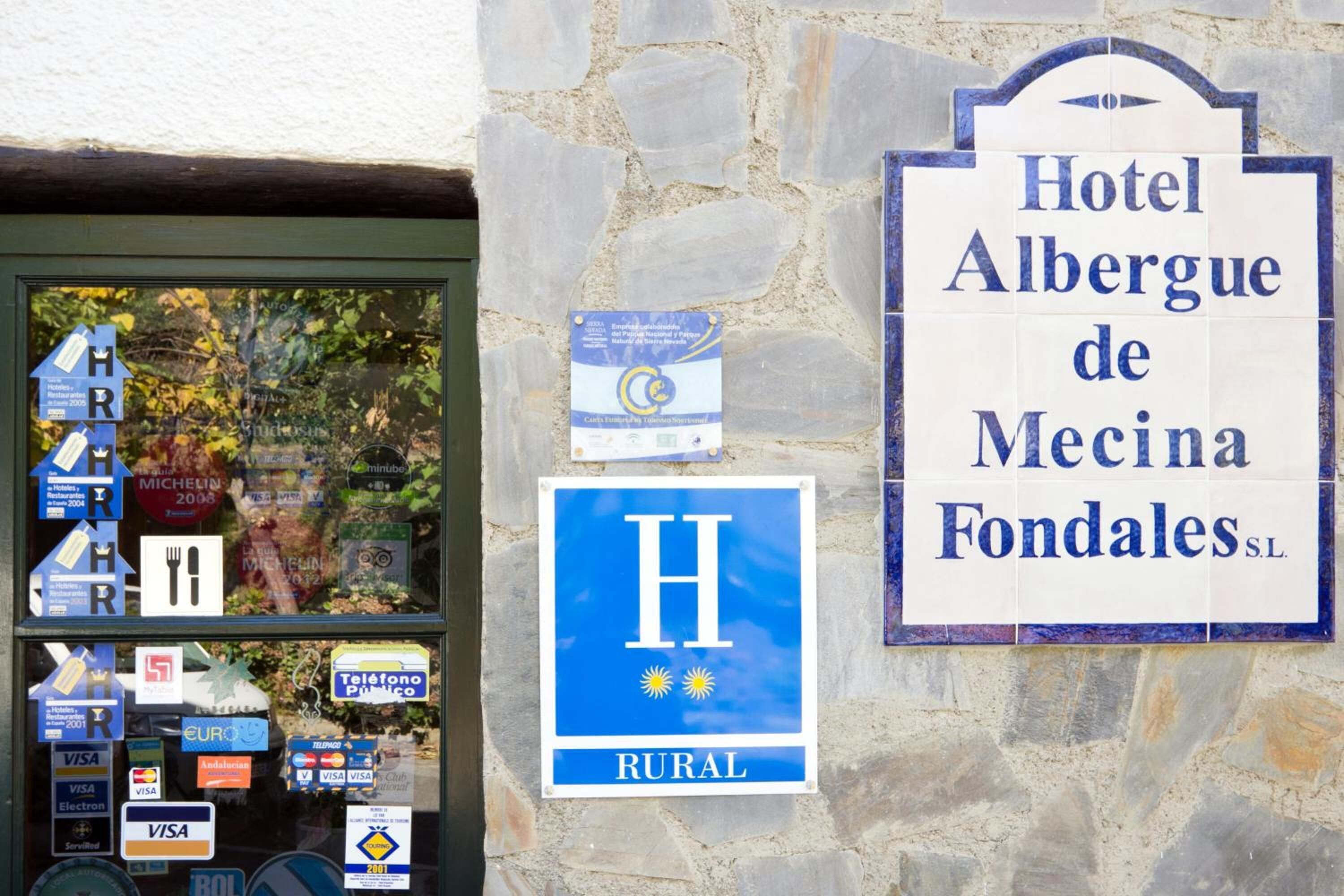 Letrero de hotel para 'Hotel Albergue de Mecina Fondales SL' y una vitrina con diversos servicios e indicaciones.