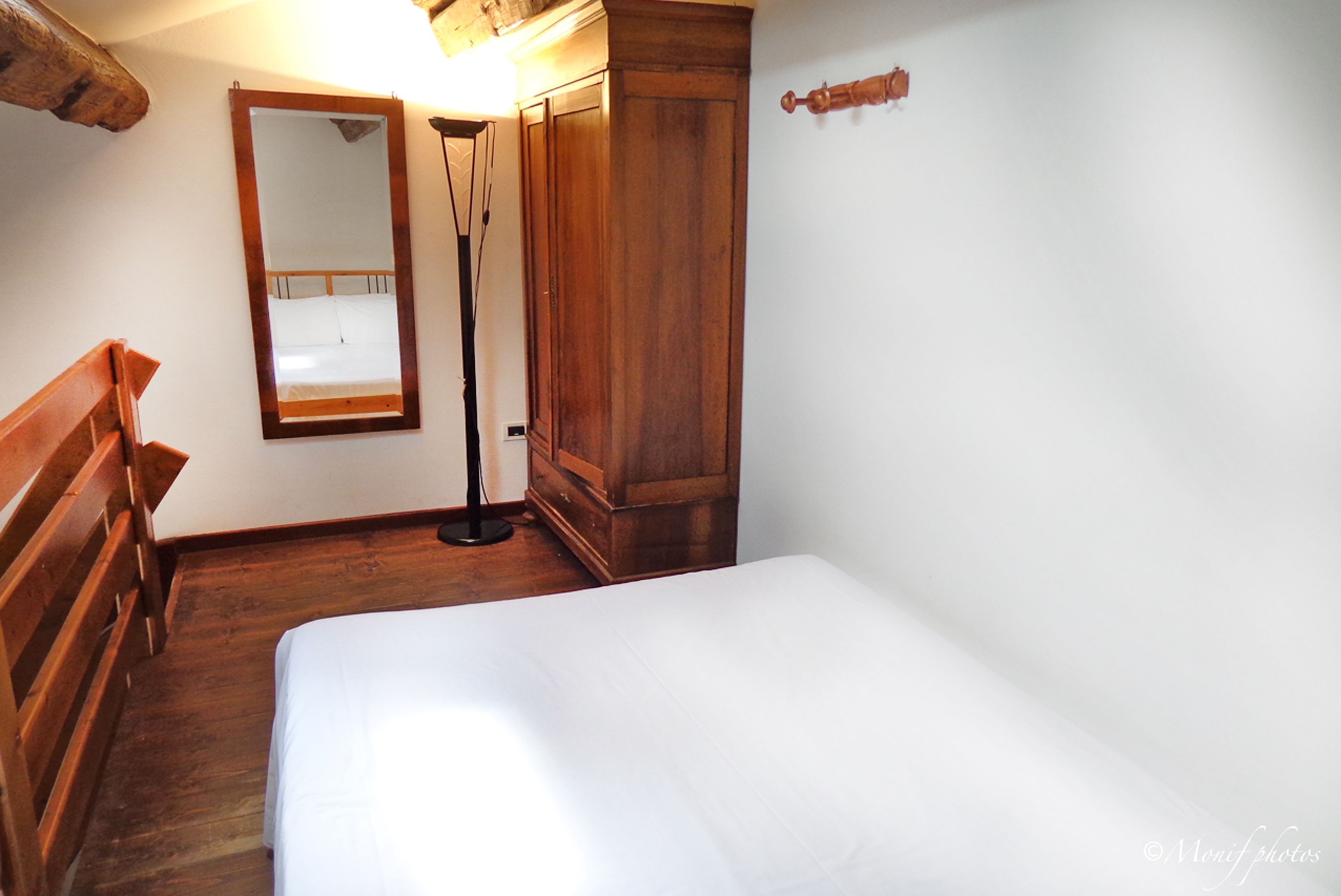 A bedroom with a wooden bed, a nightstand, a wardrobe, and a mirror.