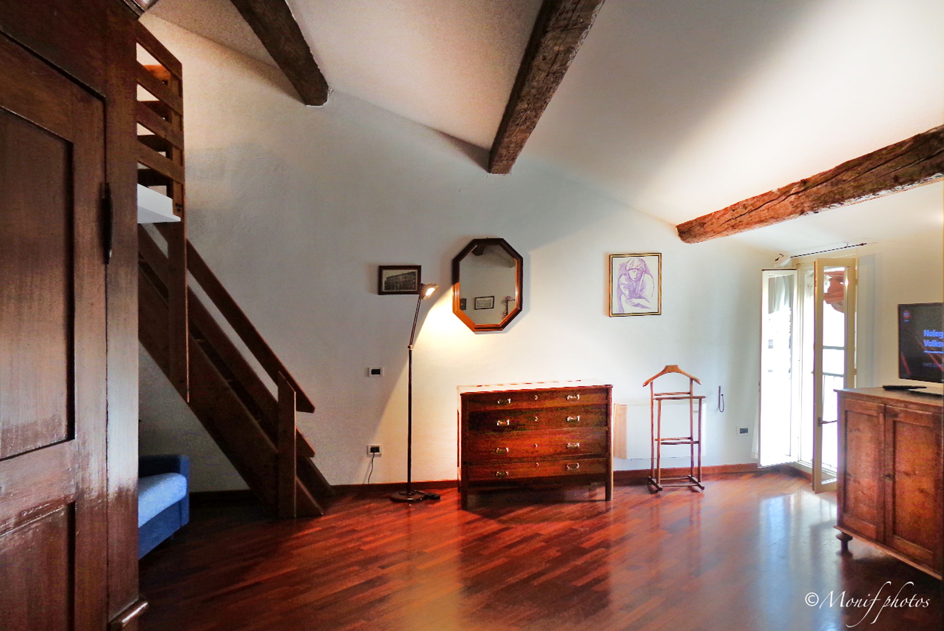 Ein geräumiges Zimmer mit Holzboden, einer Treppe, einem Schminktisch und einem Fernseher.