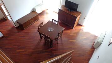 Une pièce spacieuse comprenant une table à manger en bois, des chaises, un banc, un téléviseur posé sur un meuble en bois et un escalier menant à un autre niveau.