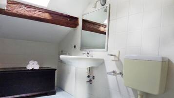 Ein Badezimmer mit weißem Waschbecken, einem Spiegel, einer Toilette und einer dunklen Holzbank.