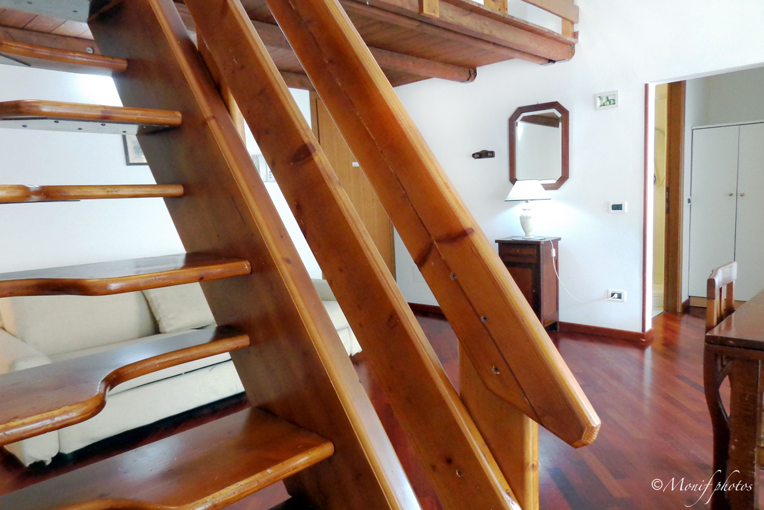A wooden staircase in a room with a white wall and a mirror.