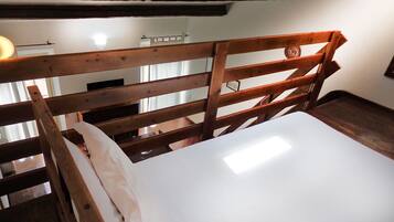 Un cadre de lit en bois avec un matelas blanc, dans une pièce dont on peut voir les poutres apparentes et qui possède un mur blanc.