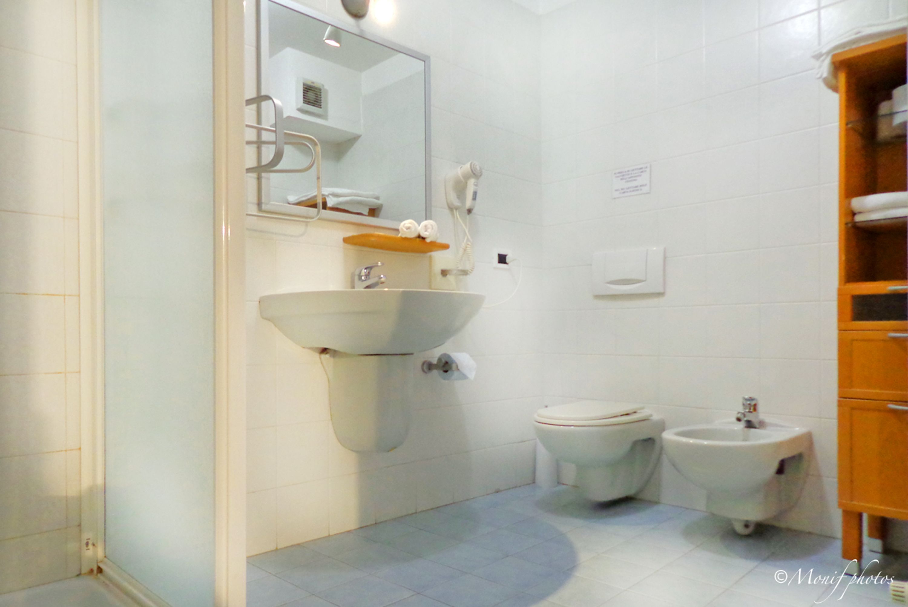 A bathroom with a sink, two toilets, a bidet, a mirror, and a towel rack.