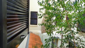 A narrow alleyway with a black metal gate, a small window with shutters, and a tree with green leaves. - Locanda della Biscia (Ferrara)