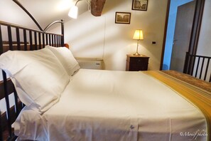 A neatly made bed with white linens in a room with a wooden headboard and a nightstand with a lamp.
