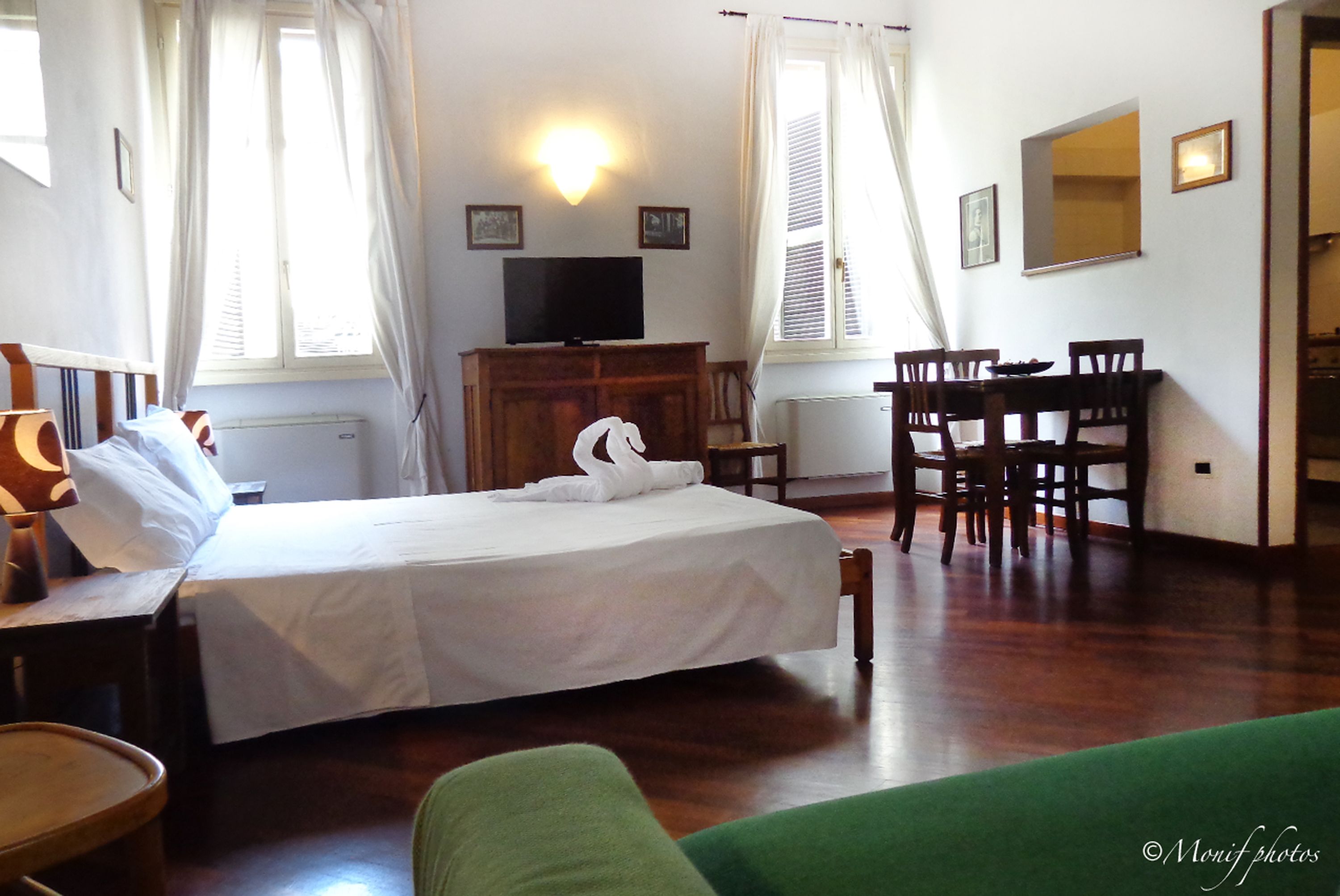 Ein Hotelzimmer mit Bett, Schreibtisch, Sessel, Fernseher und Esstisch.