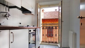 A kitchen with white cabinets, a stainless steel range hood, and an oven. A glass door leads to a balcony with a red-tiled roof. - Locanda della Biscia (Ferrara)