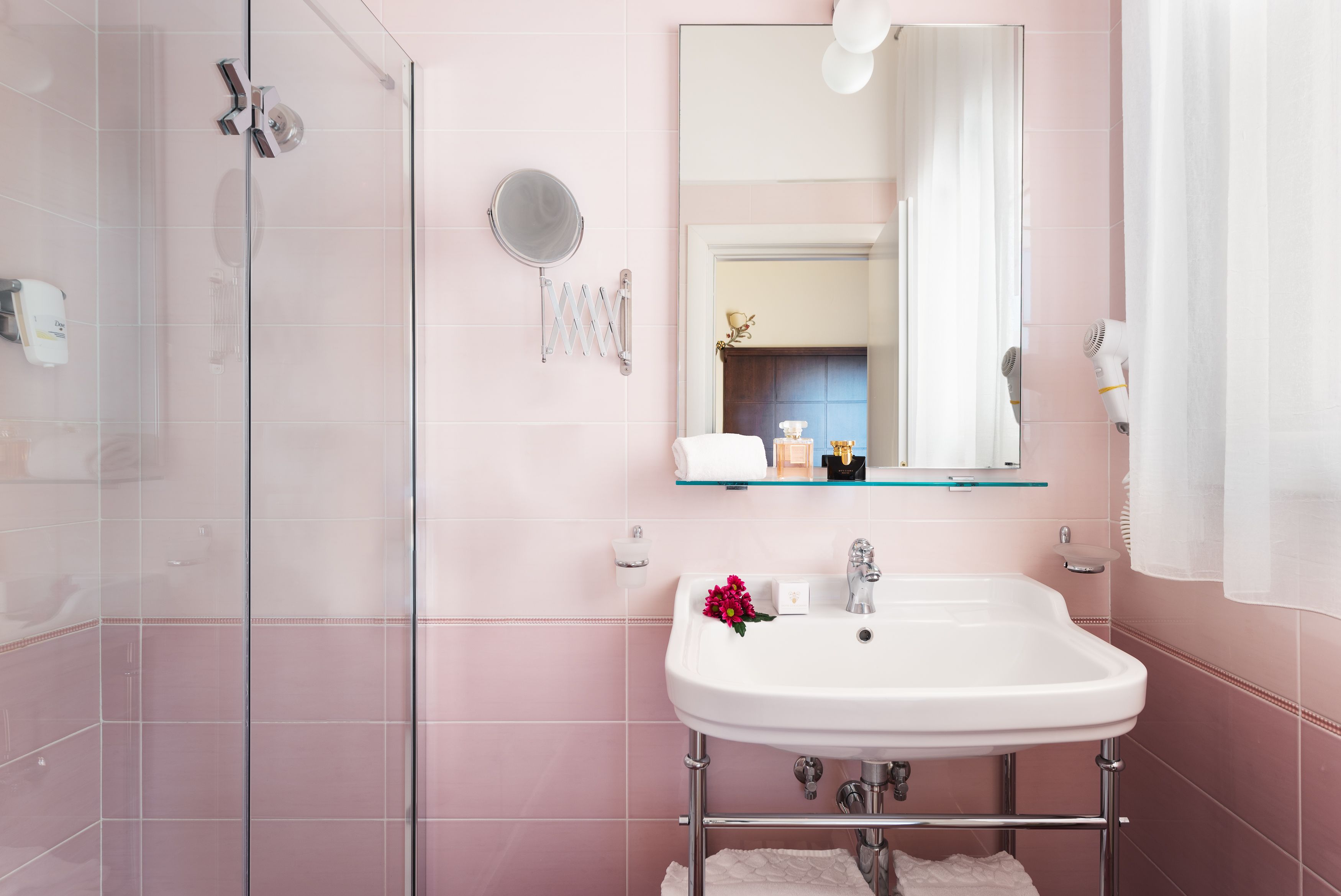 Un baño con cabina de ducha de vidrio, un lavabo blanco con un espejo encima y un perchero para toallas.