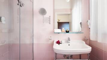 Un baño con cabina de ducha de vidrio, un lavabo blanco con un espejo encima y un perchero para toallas.
