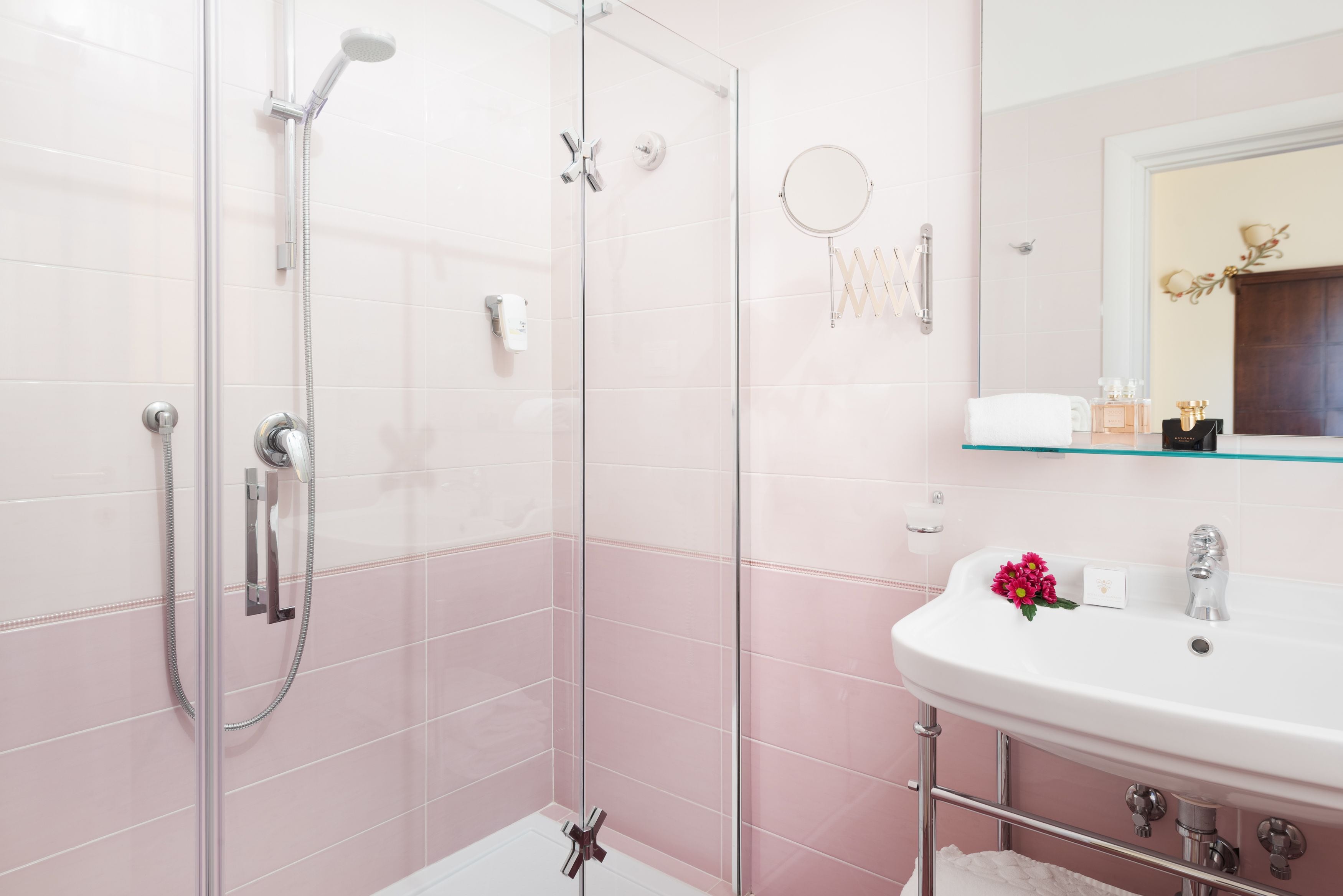 Une salle de bain moderne avec une douche à parois de verre, un lavabo blanc orné d’une fleur et un miroir au-dessus du lavabo.