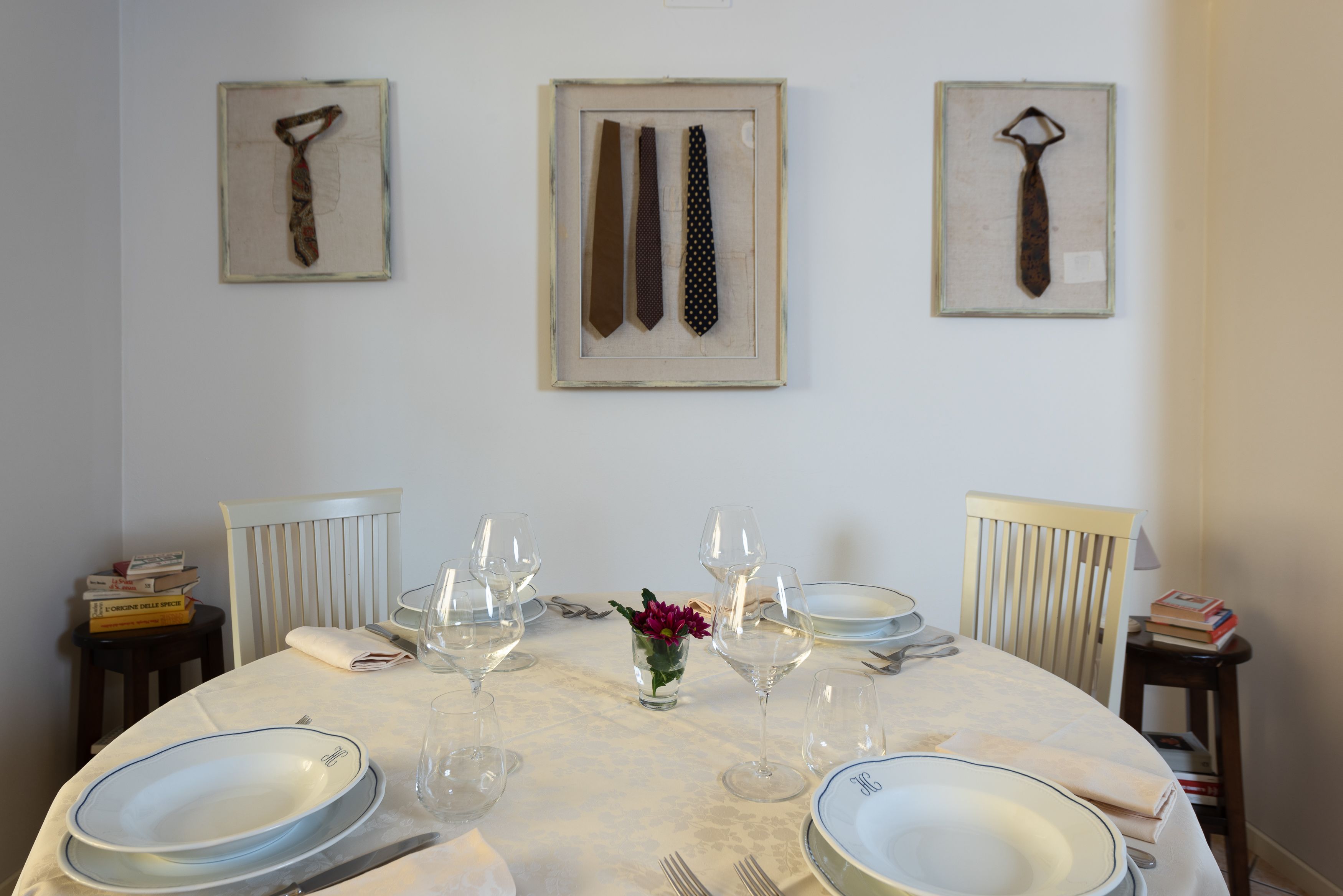 A dining table set with plates, glasses, and cutlery, flanked by chairs, with framed neckties on the wall.
