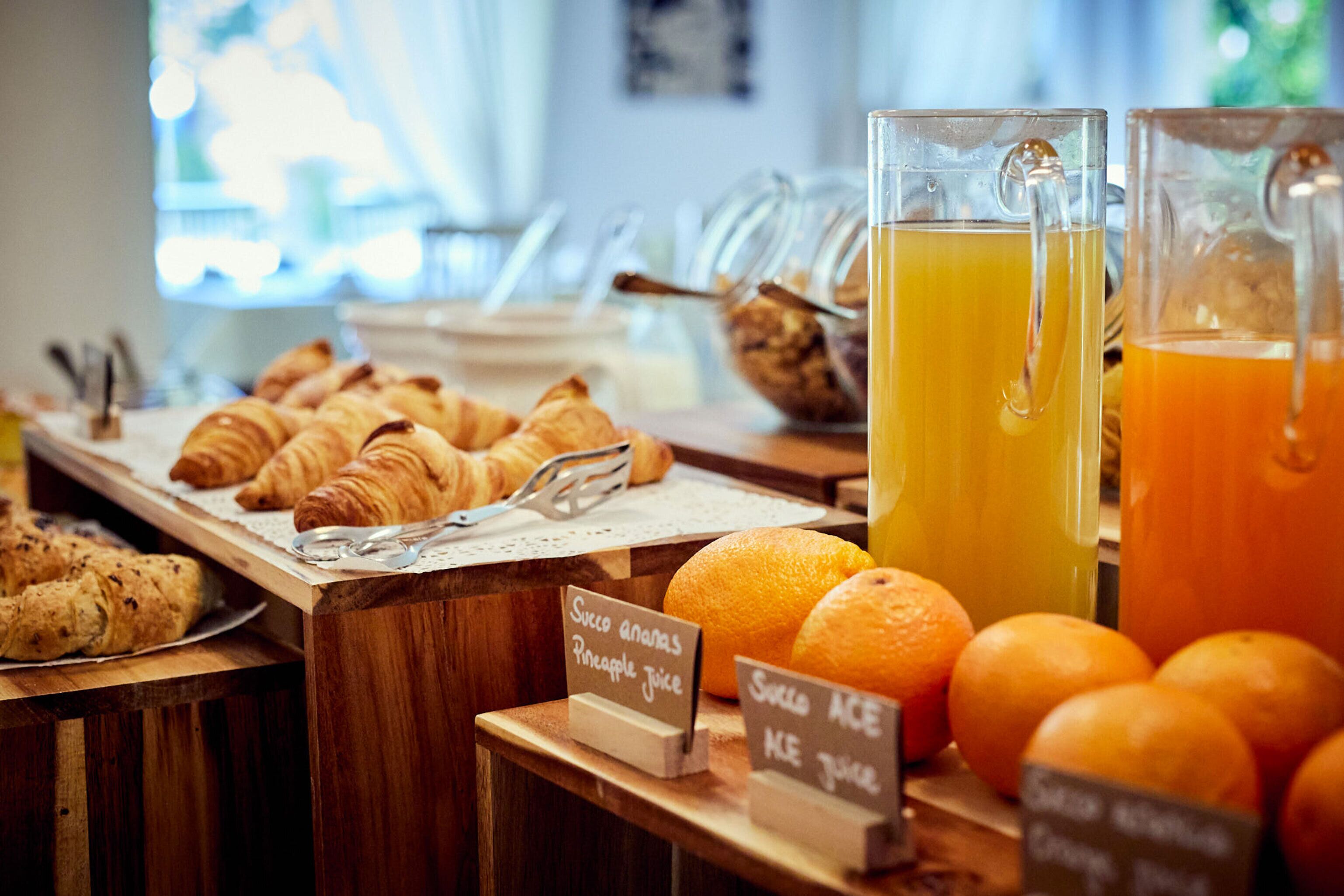 Un buffet de petit-déjeuner avec des croissants, du jus d’orange et du jus d’ananas.