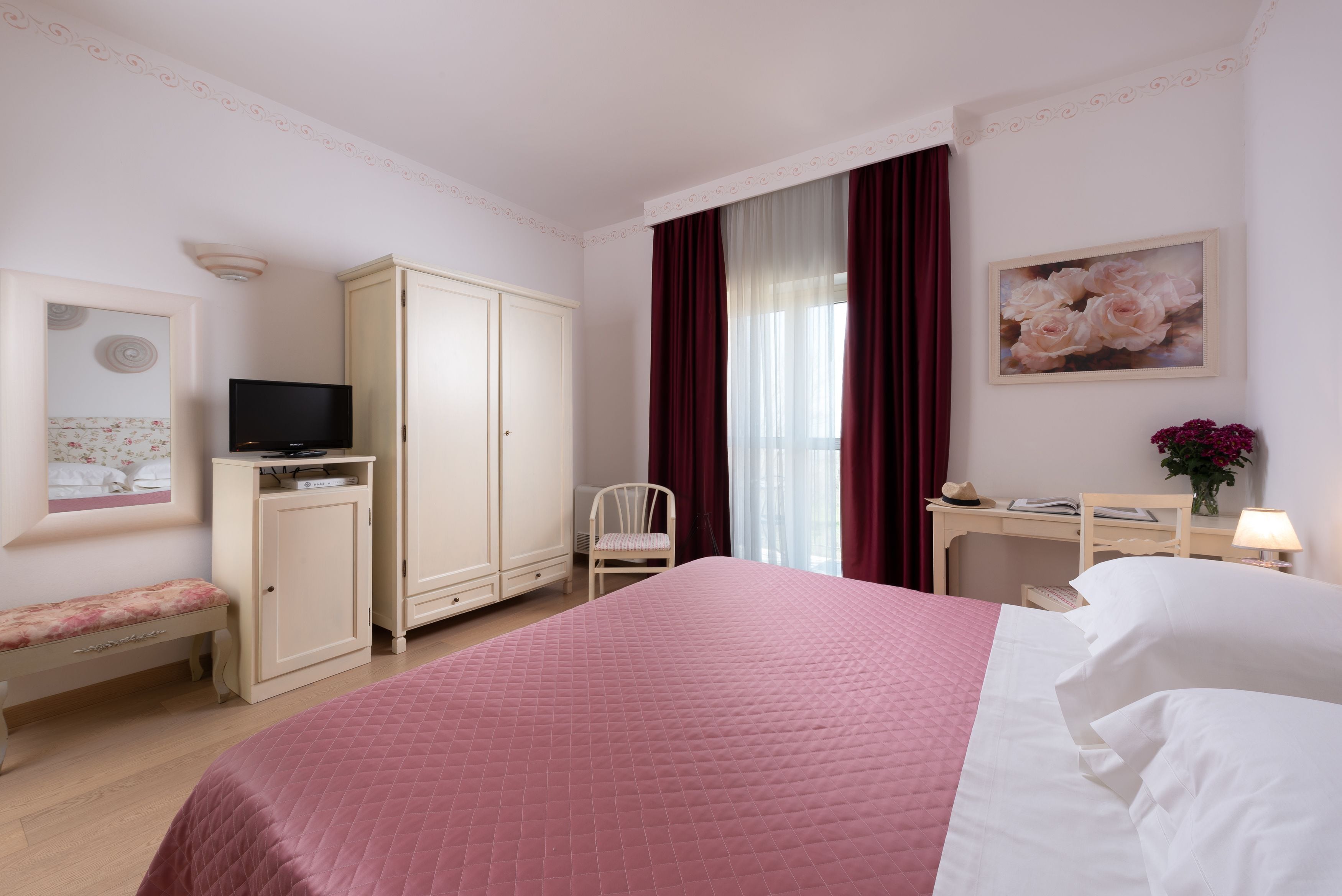 Une chambre d’hôtel comprenant un lit, un bureau, une chaise, une armoire, un téléviseur et un tableau.