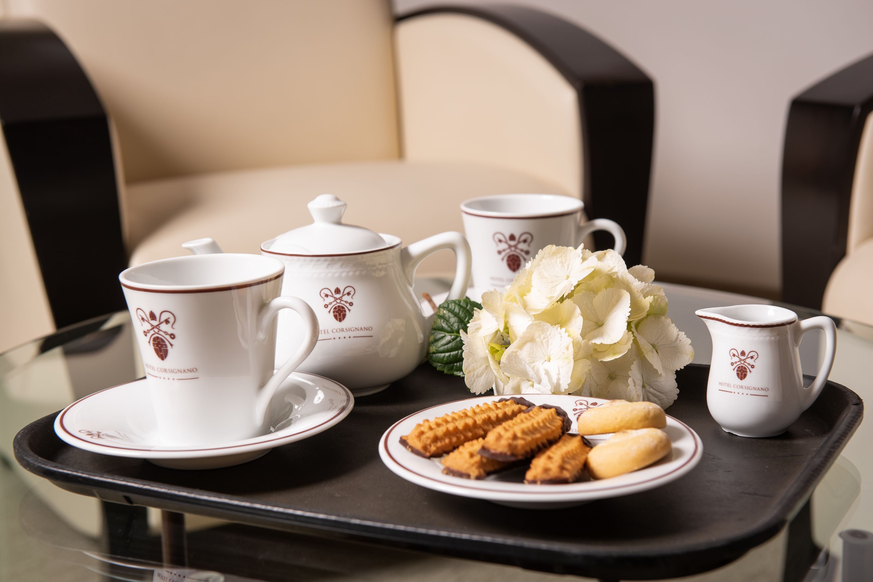A tray with a teapot, cups, a plate of biscuits, and a bouquet of flowers on a table.