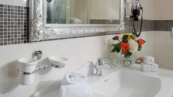 Un baño con un lavamanos blanco, un espejo, una toalla y un florero con flores.