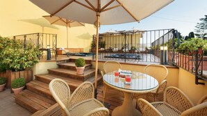 A patio area with wicker furniture, a glass table, and a pool in the background. - Hotel Corsignano (Pienza)