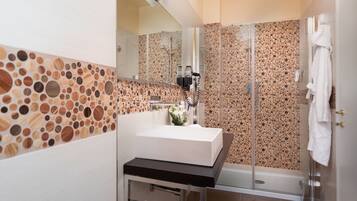Un baño moderno con un lavabo blanco, cabina de ducha con mampara de vidrio y pared revestida de mosaicos.