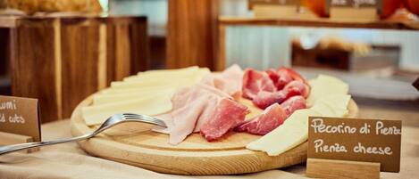 A wooden board with various cheeses and meats, accompanied by a fork and signs indicating types of cheese.