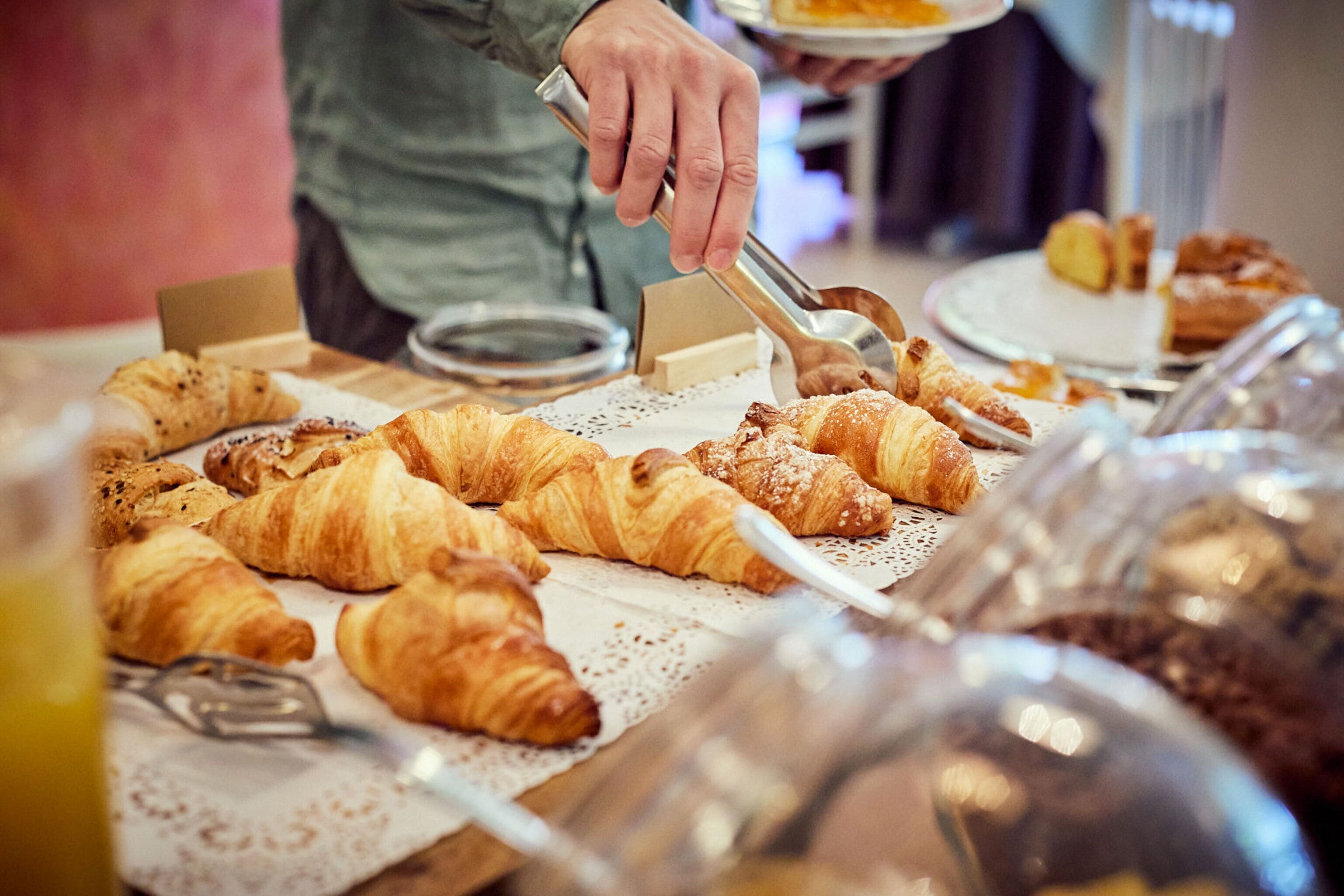 A buffet with various pastries and a person serving food.