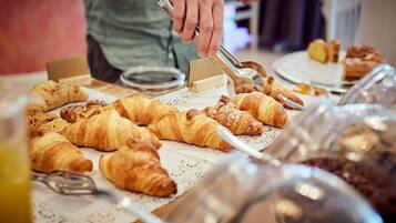 A buffet with various pastries and a person serving food.