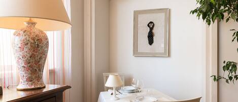 A dining area with a table set for two, a vase, and a framed picture on the wall.