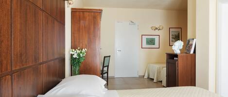 Un dormitorio con un armario de madera, una cama con ropa de cama blanca, un escritorio con silla y una puerta que da a otra habitación.
