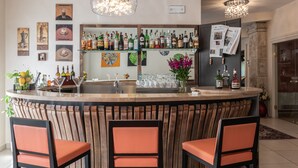 A bar area with a wooden bar counter, three orange chairs, and a variety of bottles and glasses. - Hotel Corsignano (Pienza)
